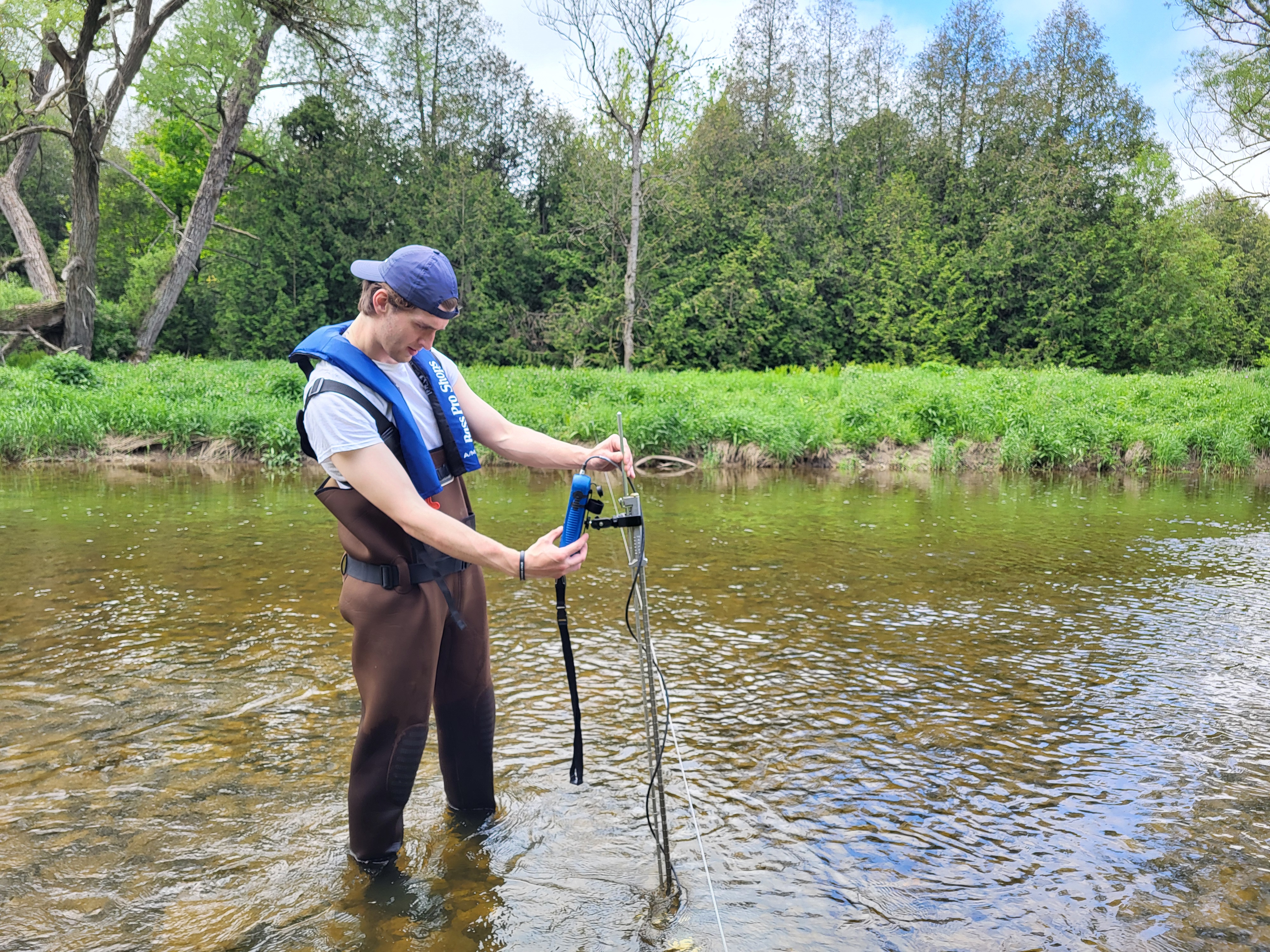 Staff in lifejacket and waders in river with equipment